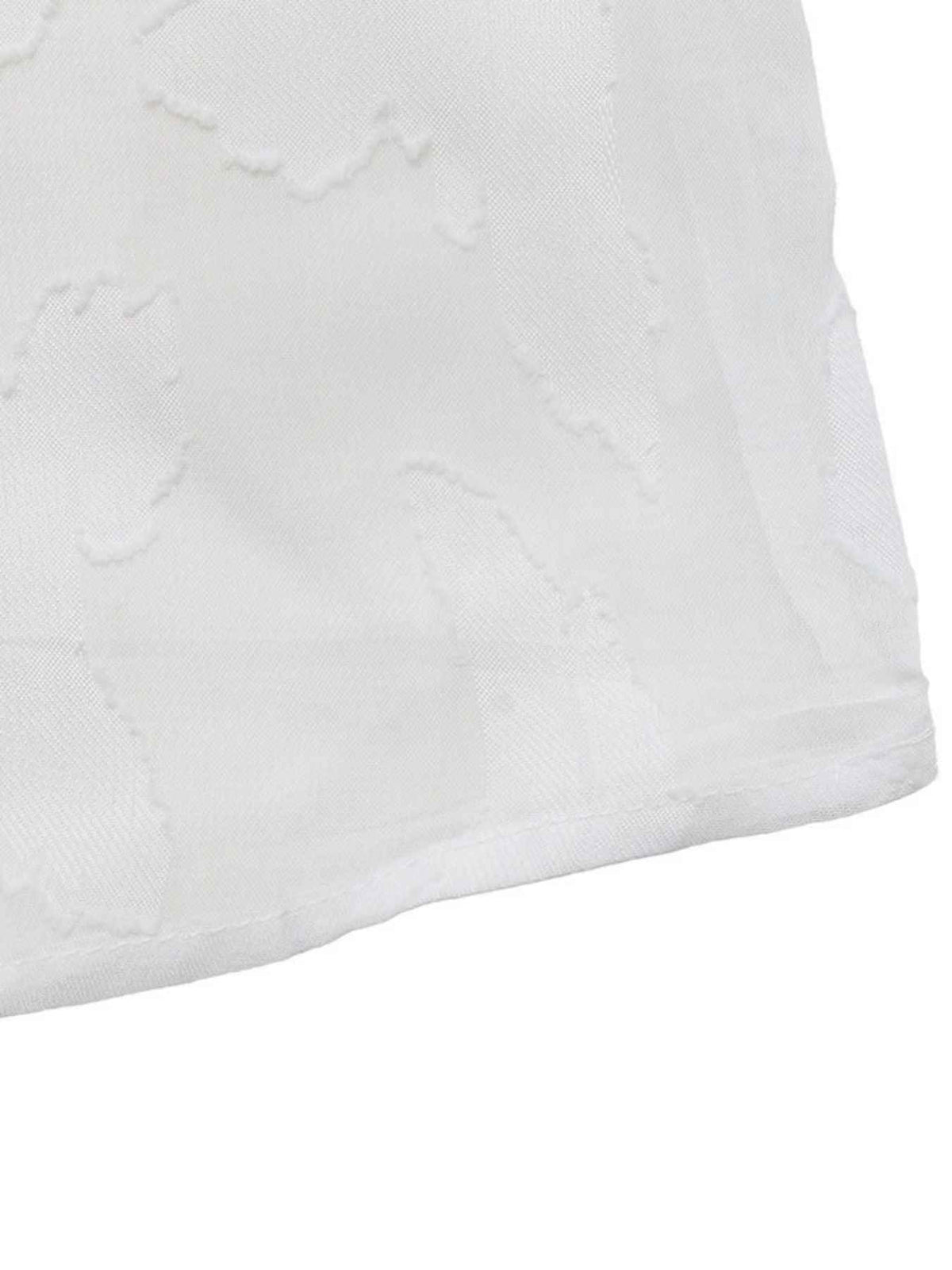 Close-up of a white textured fabric with a subtle embossed or woven floral pattern, showing the fabric's fine weave and stitched edge against a white background.