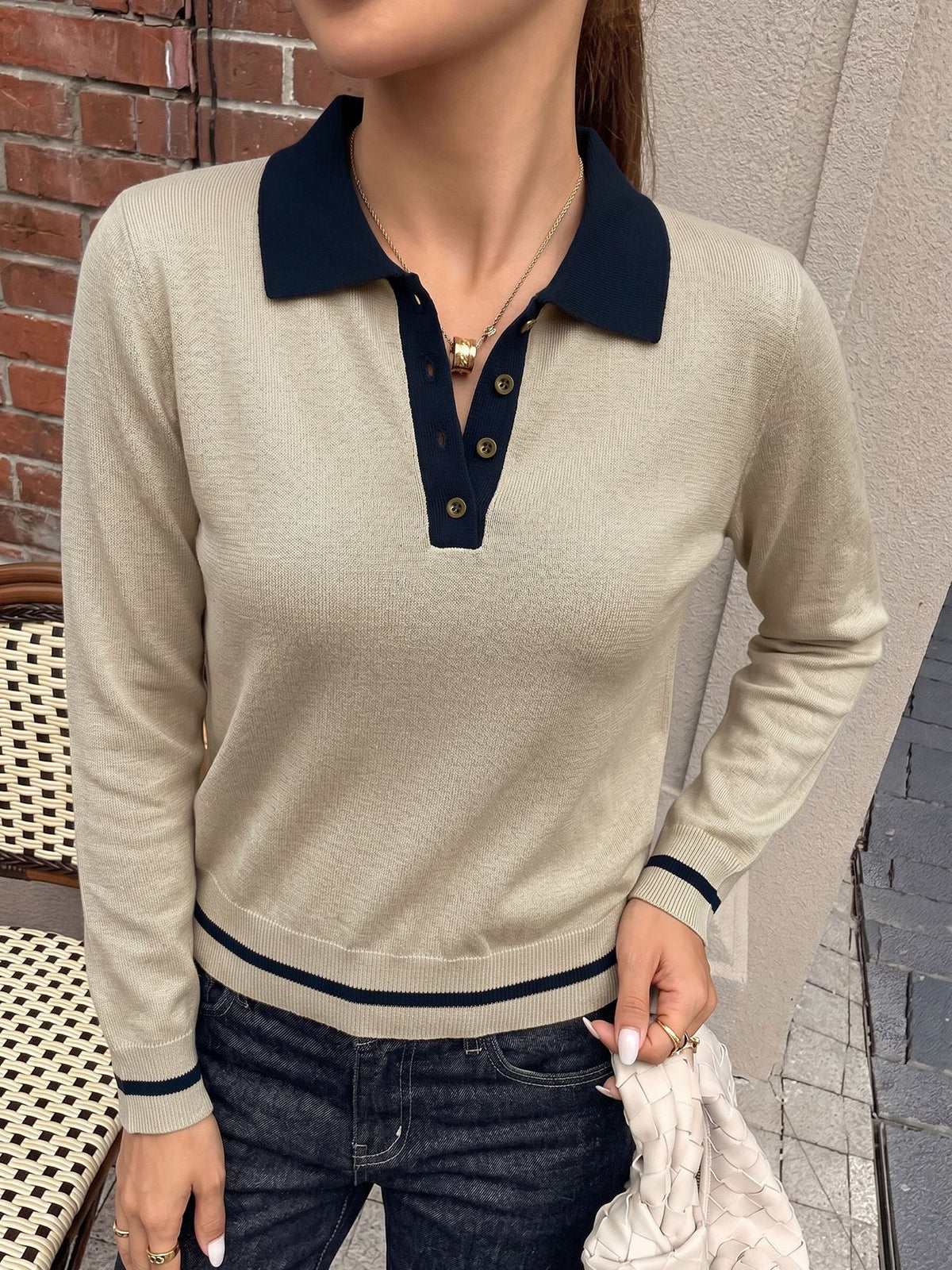A woman wearing a beige long-sleeve polo sweater with a contrasting dark navy collar, button placket, and ribbed cuffs and hem, paired with dark blue jeans.