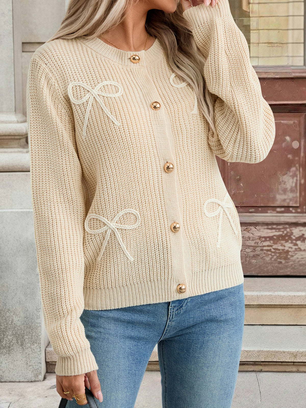 Beige knitted cardigan with bow details worn by a person, standing against a neutral background.