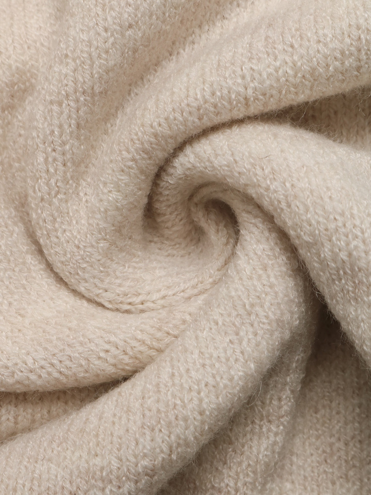 A close-up of soft, textured knit fabric in a warm off-white or cream tone, arranged in a spiral drape to show the material's fine weave and plushness.