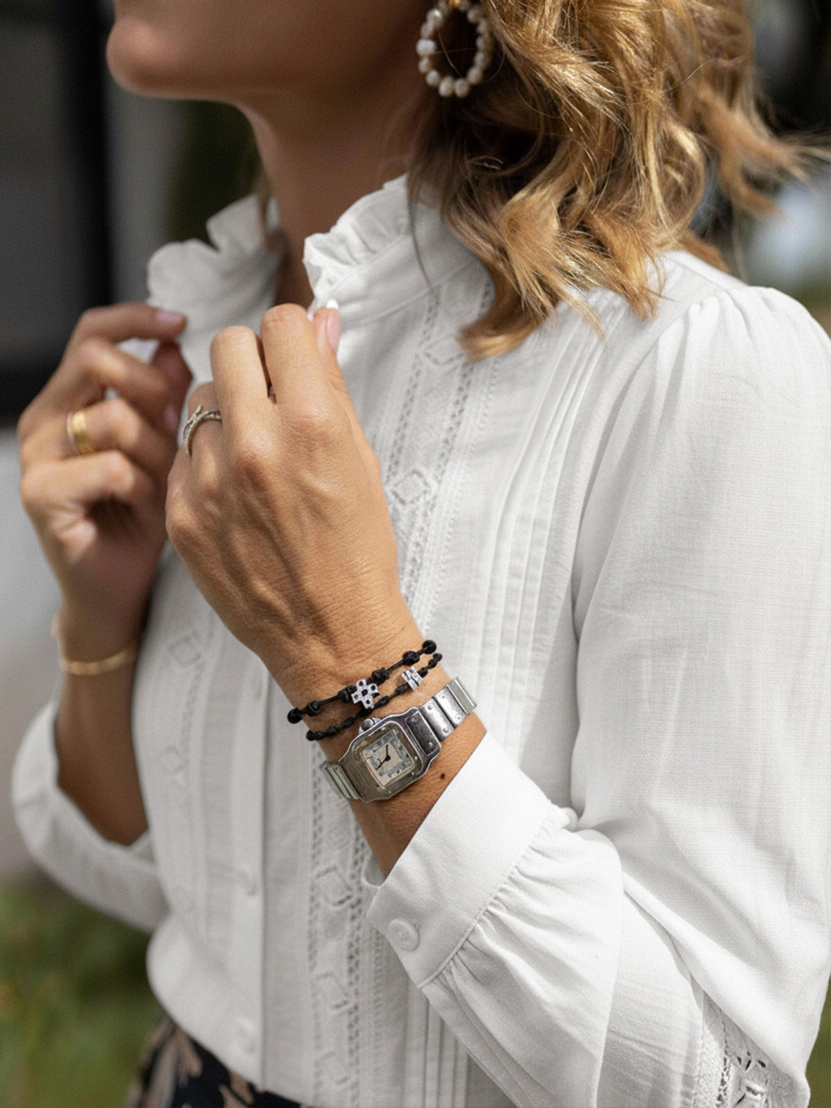 Close-up of a person wearing a white blouse with visible jewelry including a watch and bracelets.