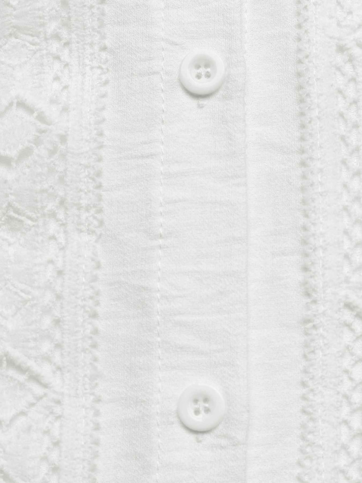Close-up of a white textured button-up shirt showing vertical embroidered or lace-like panels and two white buttons.