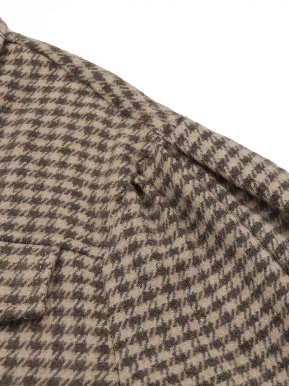 Close-up of a houndstooth patterned fabric in beige and dark brown, showing the texture and a folded pocket edge against a white background.