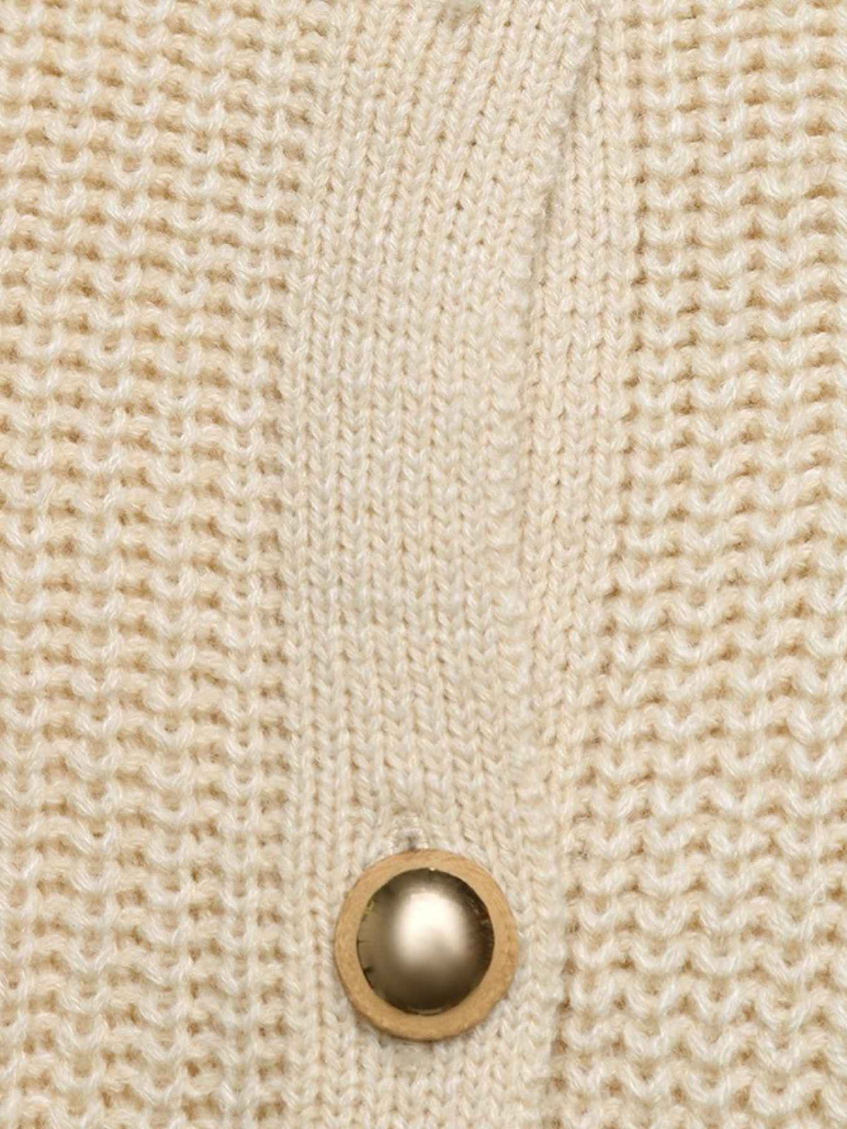 Close-up of a cream-colored chunky knit cardigan featuring a single round wooden button with a metallic gold center.