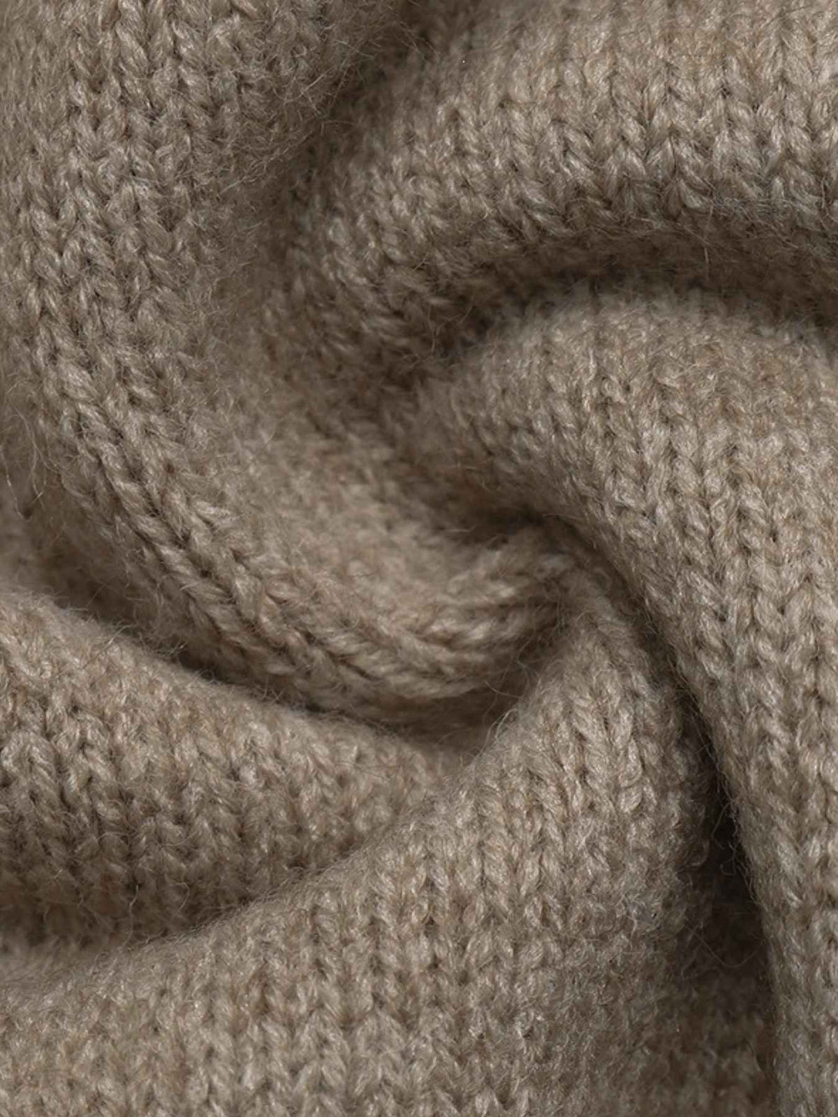 A close-up of a soft, knitted fabric in a warm taupe-beige color, arranged in a gentle spiral to show the texture and drape.