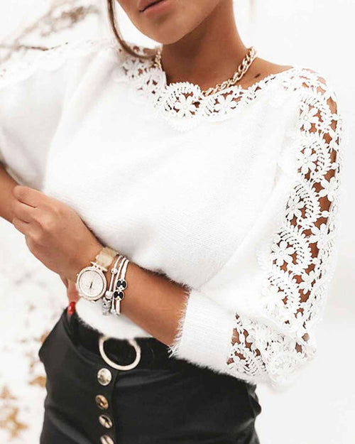 A close-up of a woman wearing a white knit sweater with intricate floral lace trim along the neckline and sleeves, paired with black high-waisted pants featuring a silver ring detail.