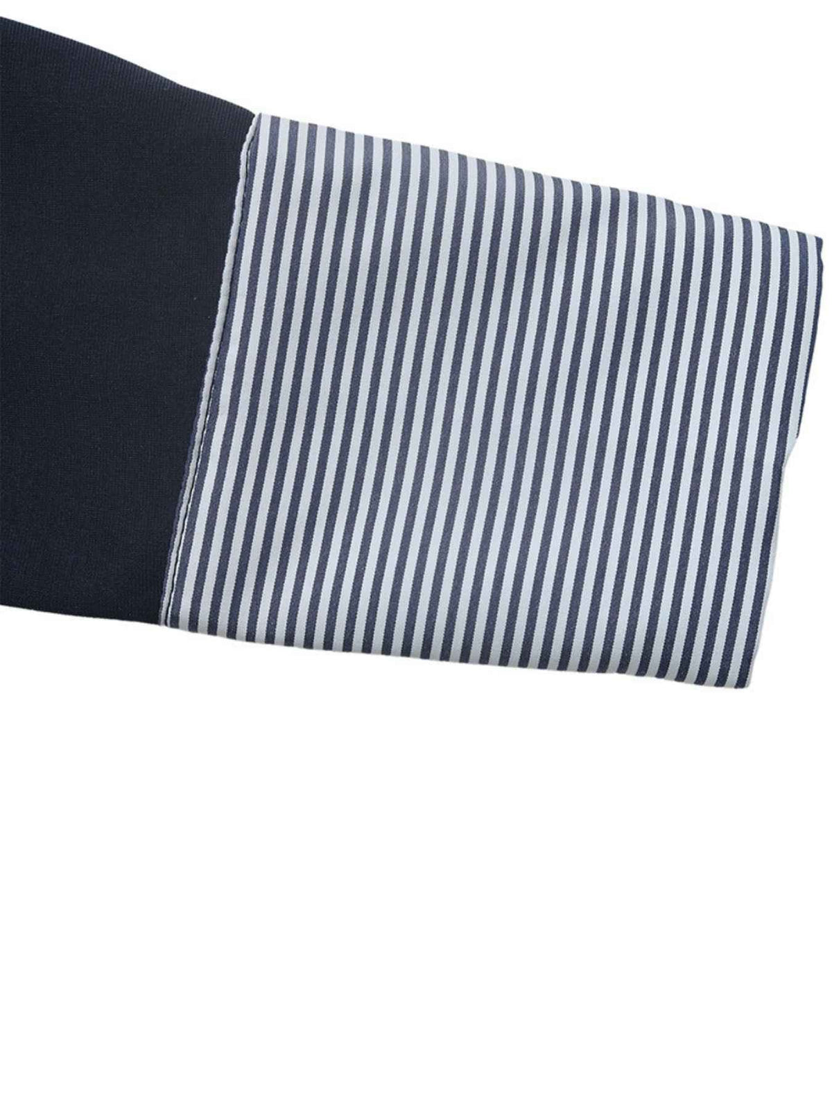 Close-up of a folded garment sleeve showing a solid black cuff section and a striped cuff section with narrow navy and white vertical stripes.