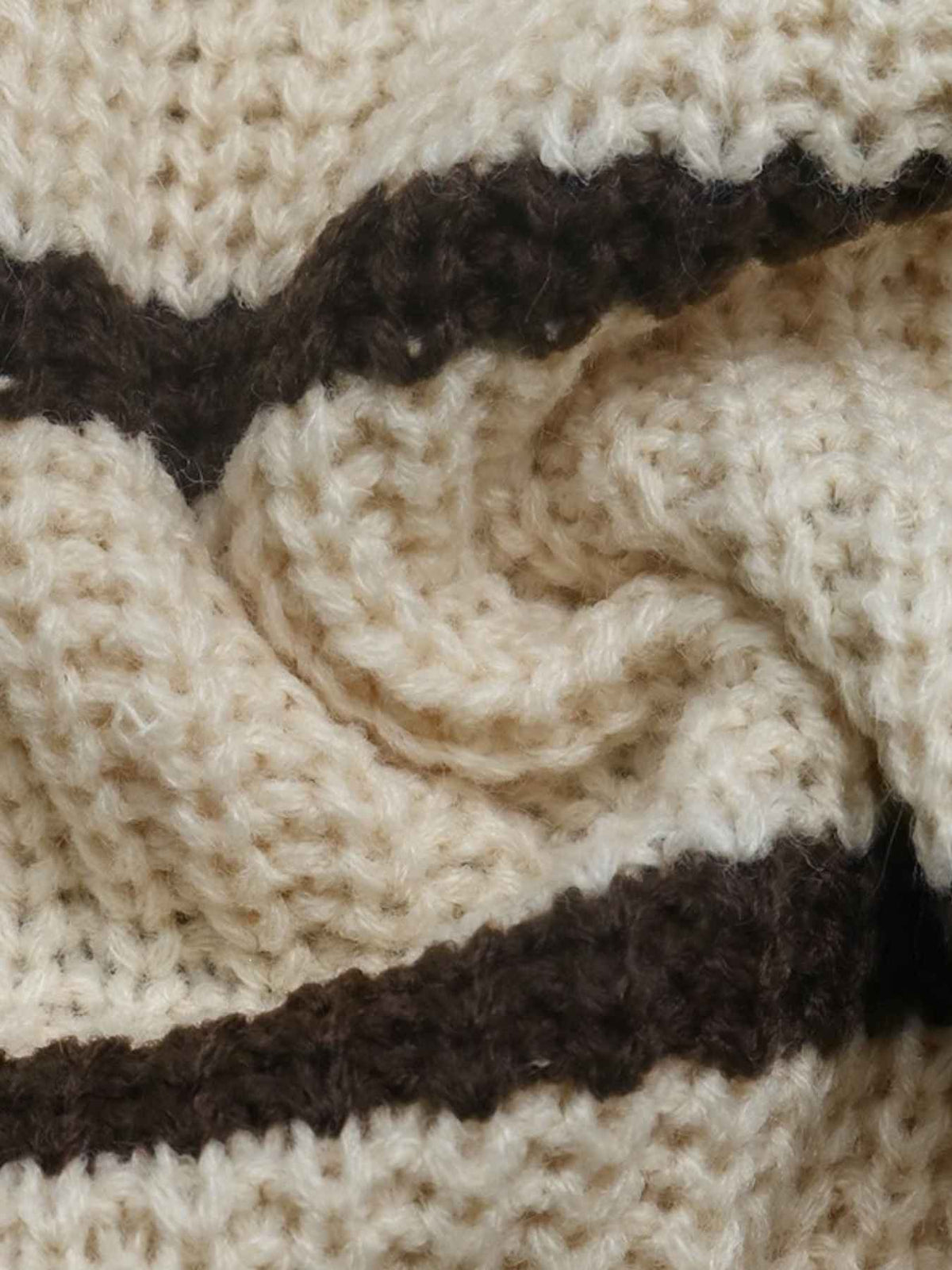 Close-up of a knitted textile with a cream base and dark brown wavy stripes, showing the texture and stitch pattern.