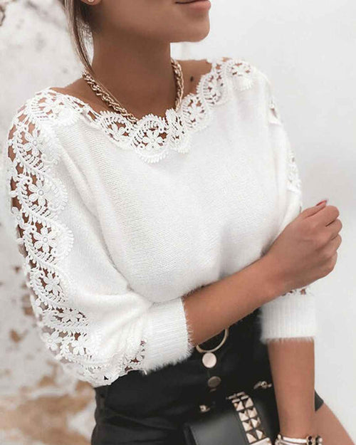 A woman wearing a white knit sweater with intricate lace trim around the crew neck and sleeves, paired with black high-waisted shorts.