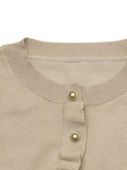 Close-up of a beige ribbed knit top with a ruffled placket and two gold-tone decorative buttons, shown against a plain white background.