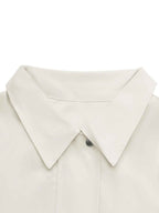Close-up of a light cream or off-white collared shirt with a pointed collar and a single dark button, shown against a plain white background.