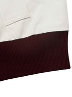 Close-up detail of a garment showing a white fabric section above a dark burgundy ribbed knit hem on a white background.