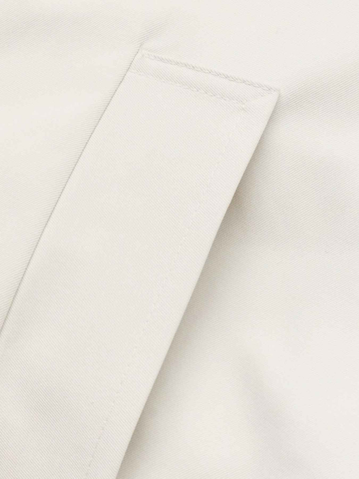 Close-up of a light cream or off-white fabric surface with a folded corner showing the texture and stitching.
