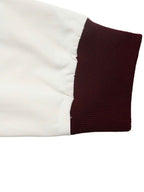 Close-up of a garment sleeve showing a solid white smooth fabric body and a ribbed dark burgundy cuff on a white background.