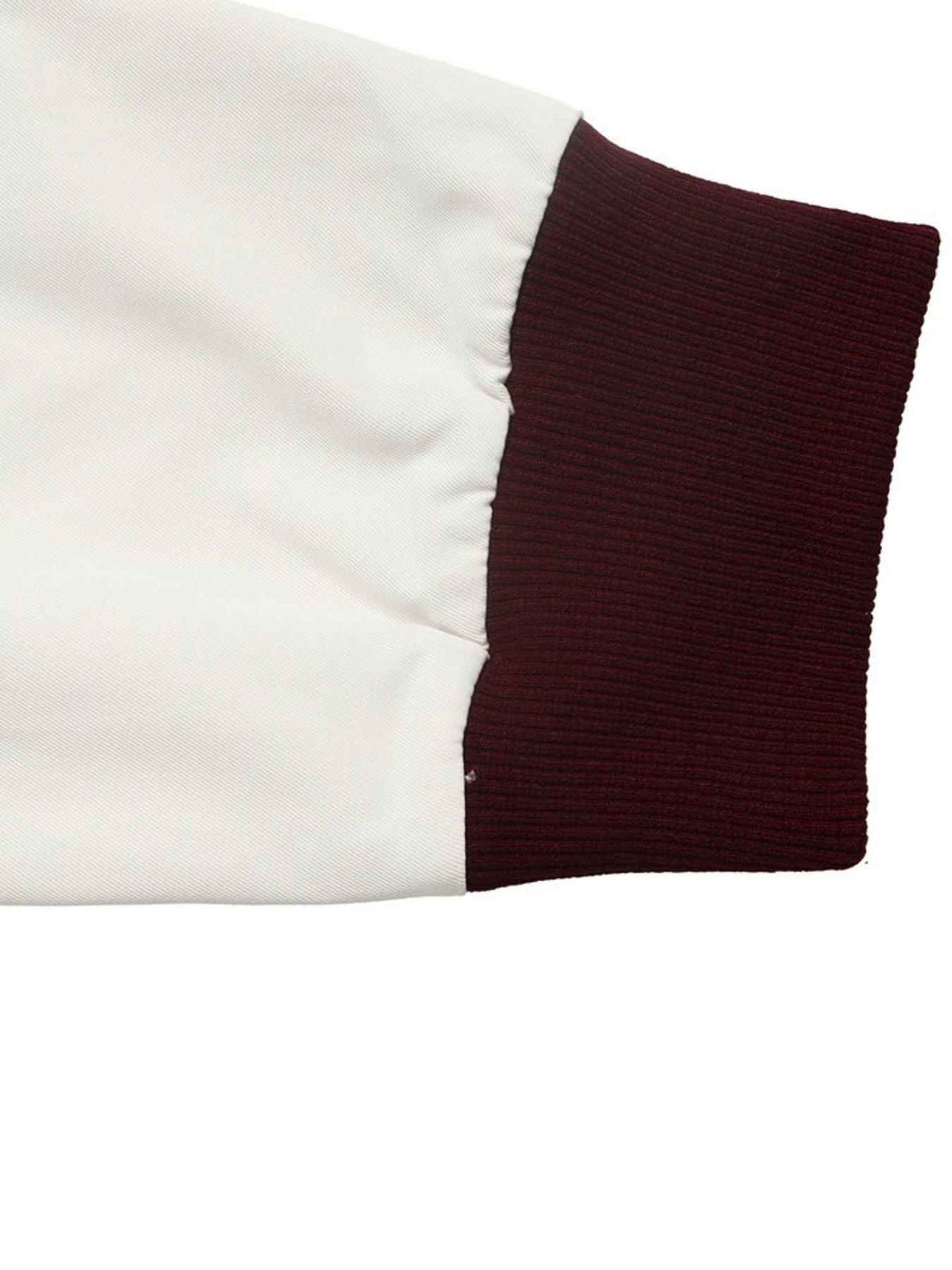 Close-up of a garment sleeve showing a solid white smooth fabric body and a ribbed dark burgundy cuff on a white background.
