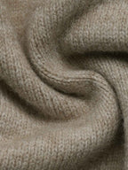 A close-up of soft, knitted fabric in a warm light beige or oatmeal tone, shown with gentle folds and texture.