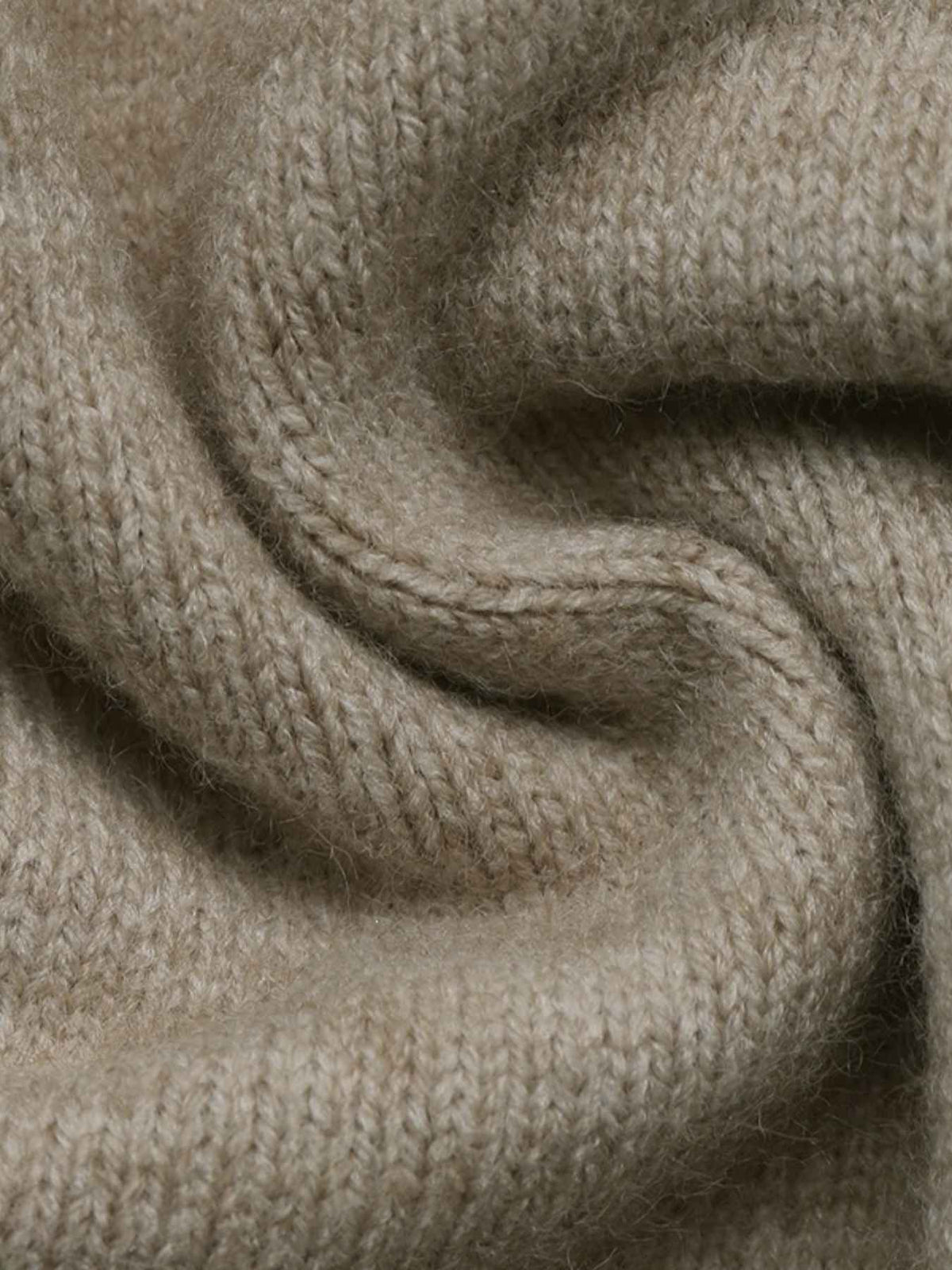 A close-up of soft, knitted fabric in a warm light beige or oatmeal tone, shown with gentle folds and texture.