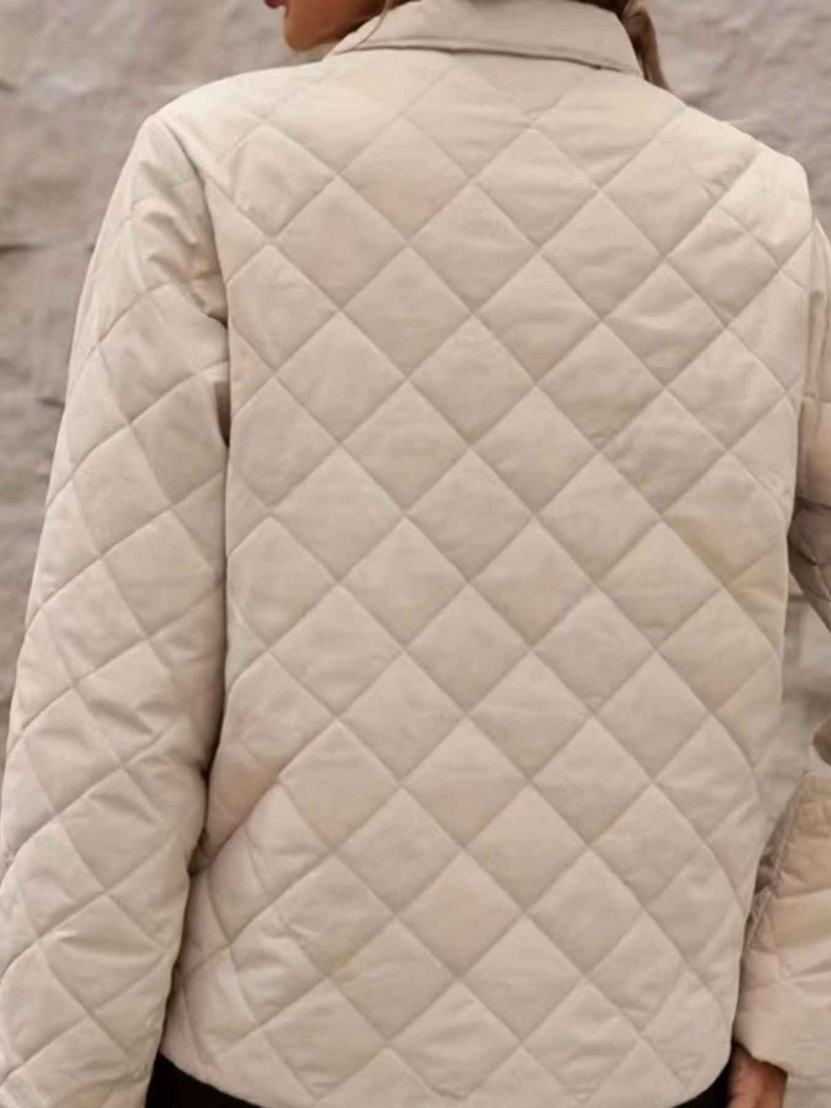 A close-up back view of a person wearing a quilted jacket in a light cream or off-white color, with a diamond-quilted pattern and a visible collar.