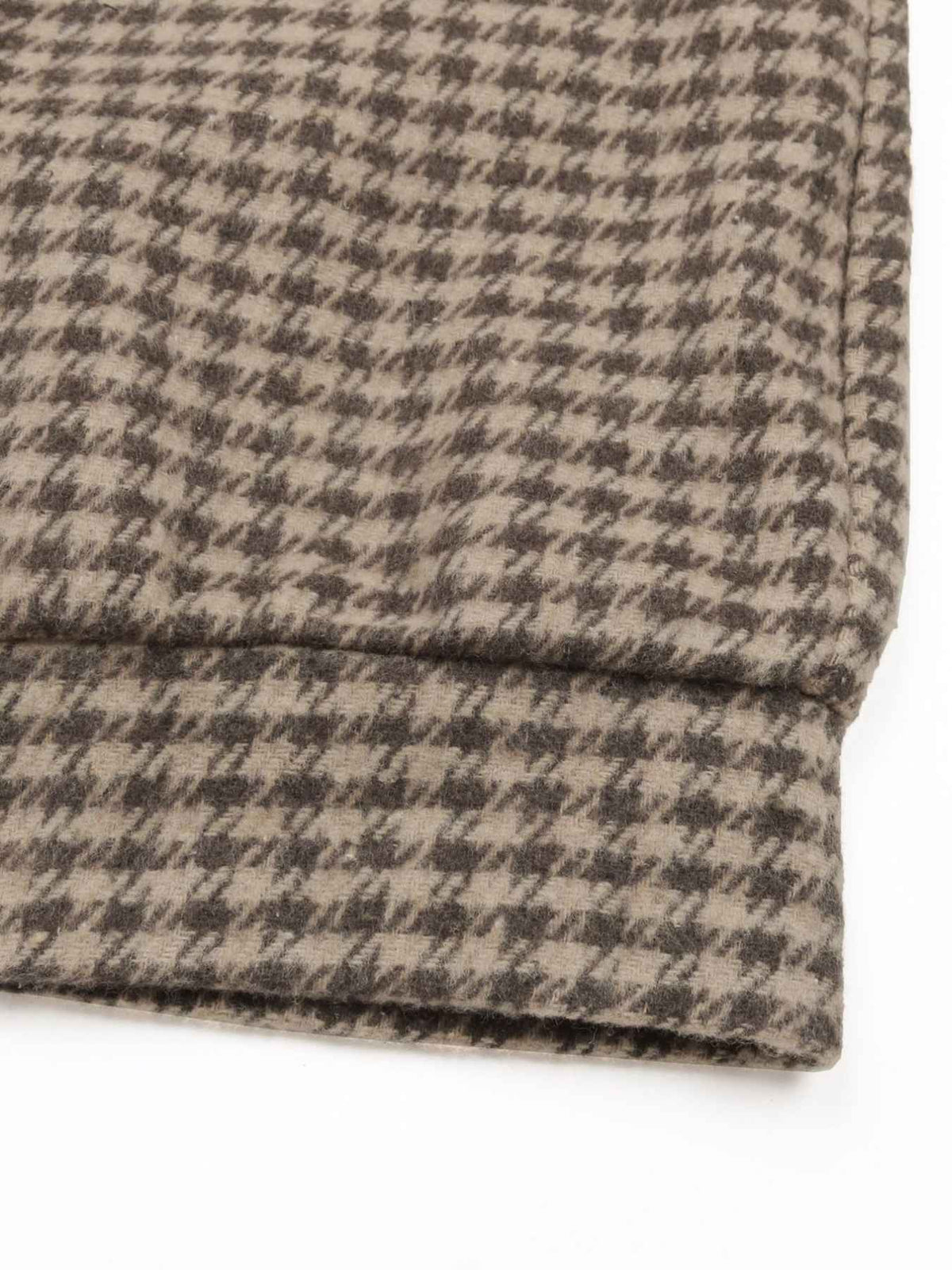 Close-up of a folded knit fabric with a small-scale houndstooth pattern in beige and dark gray, showing the texture and cuff construction on a white background.