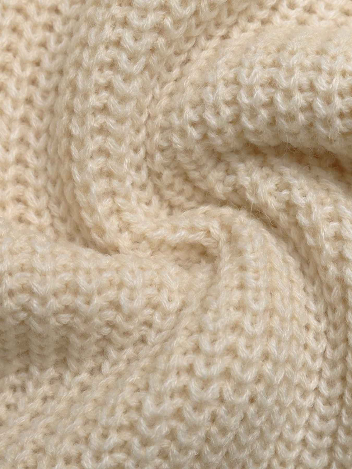 A close-up of a cream-colored, textured knit fabric with a swirled, draped pattern showing the detailed knit stitches.