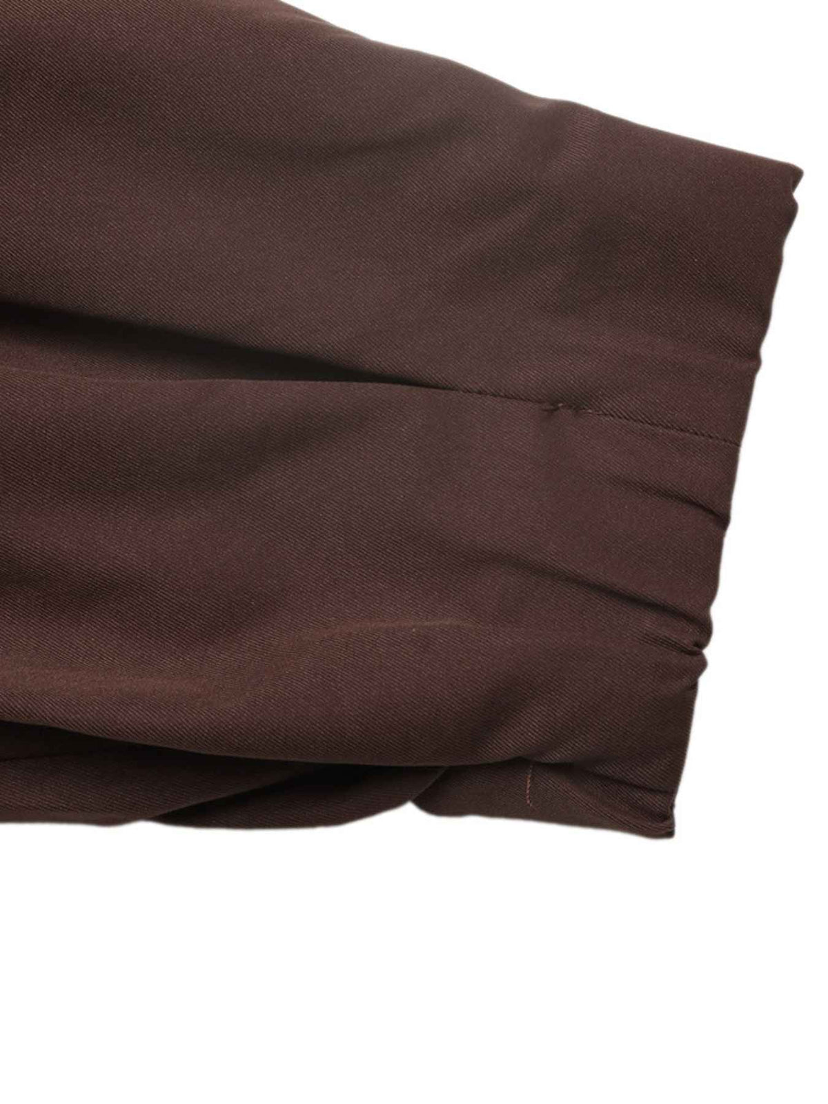A close-up of folded dark brown fabric with a visible stitched seam and gathered pleat detail, shown against a plain white background.