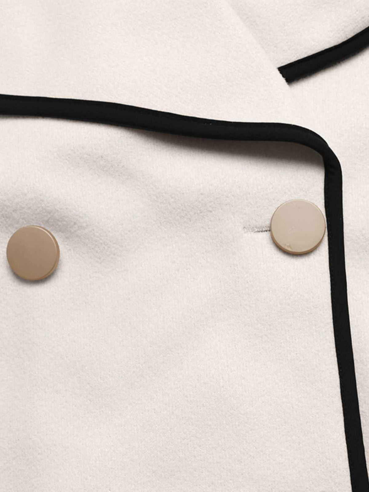 Close-up of a cream-colored coat with black piping trim and round beige buttons.