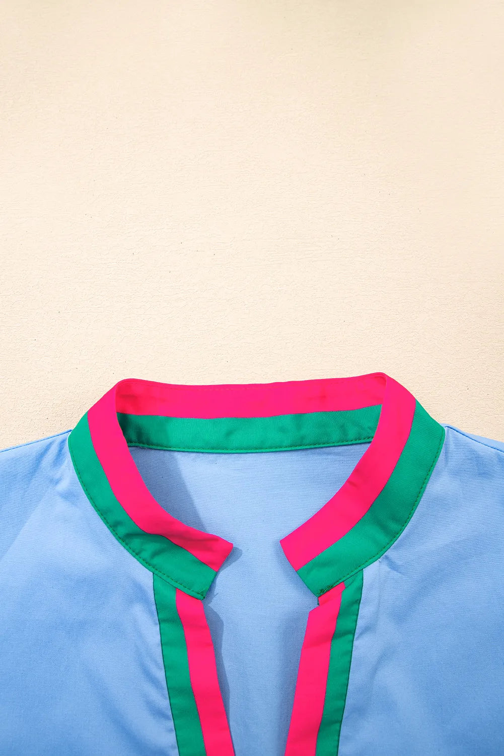 Light blue shirt with pink and green collar on a beige background