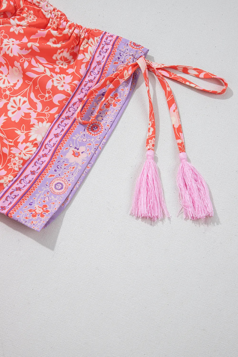 Floral-patterned belt with pink tassels on a light gray background