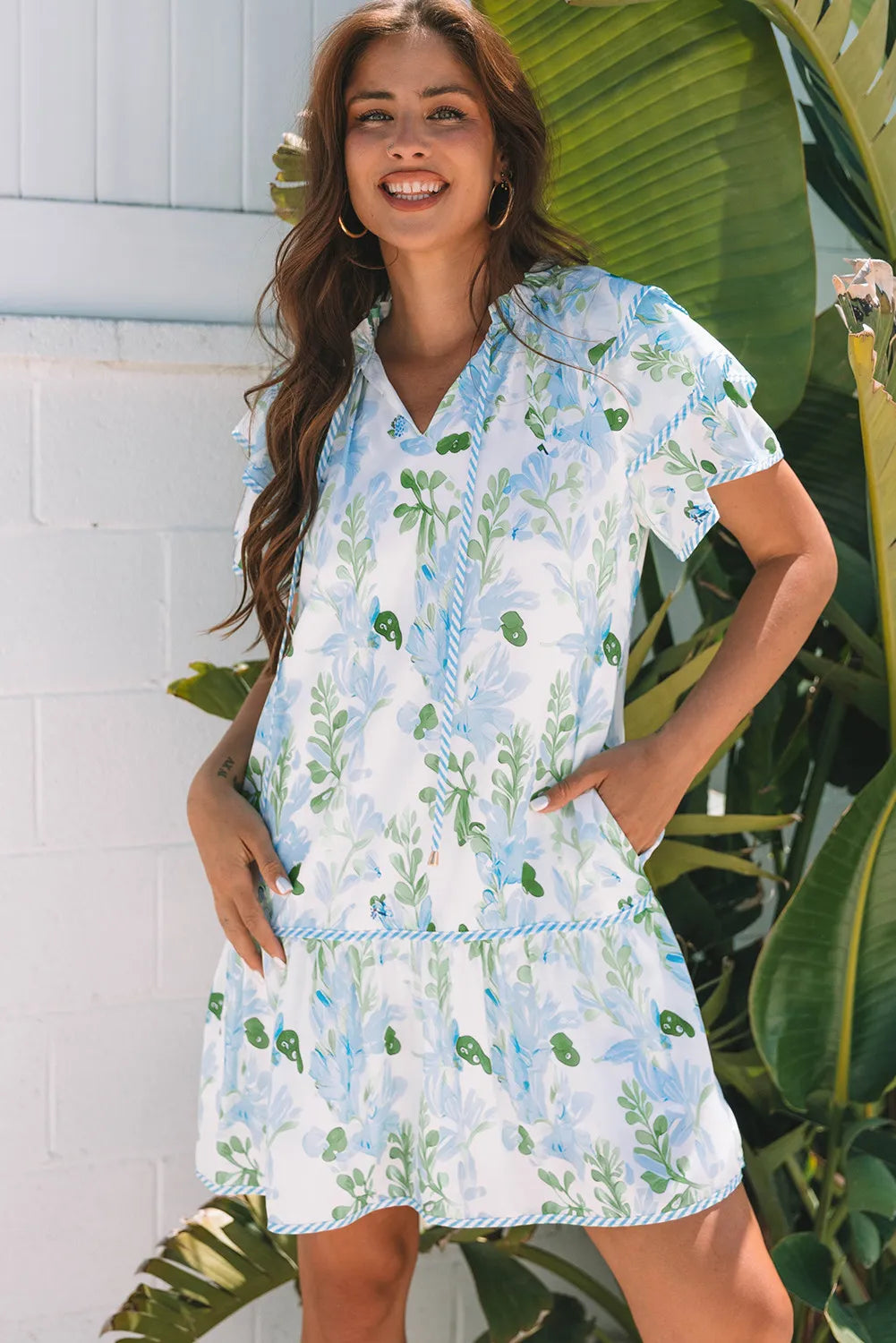 Woman wearing a floral dress standing in front of a white wall and green plants