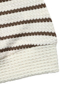 Close-up of a textured knit fabric with horizontal stripes in dark brown and off-white, showing a ribbed cuff on a plain white background.