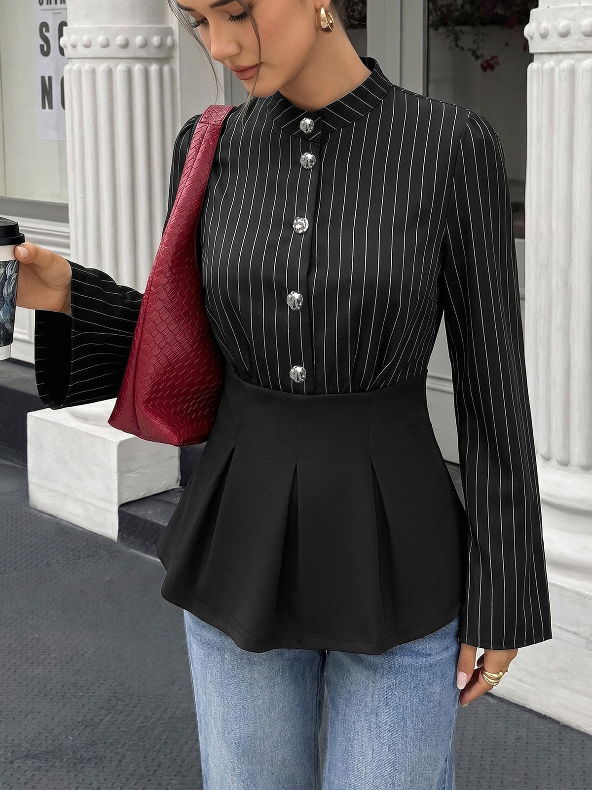 Woman wearing a black pinstripe blouse with a peplum waist, holding a red bag and a coffee cup.