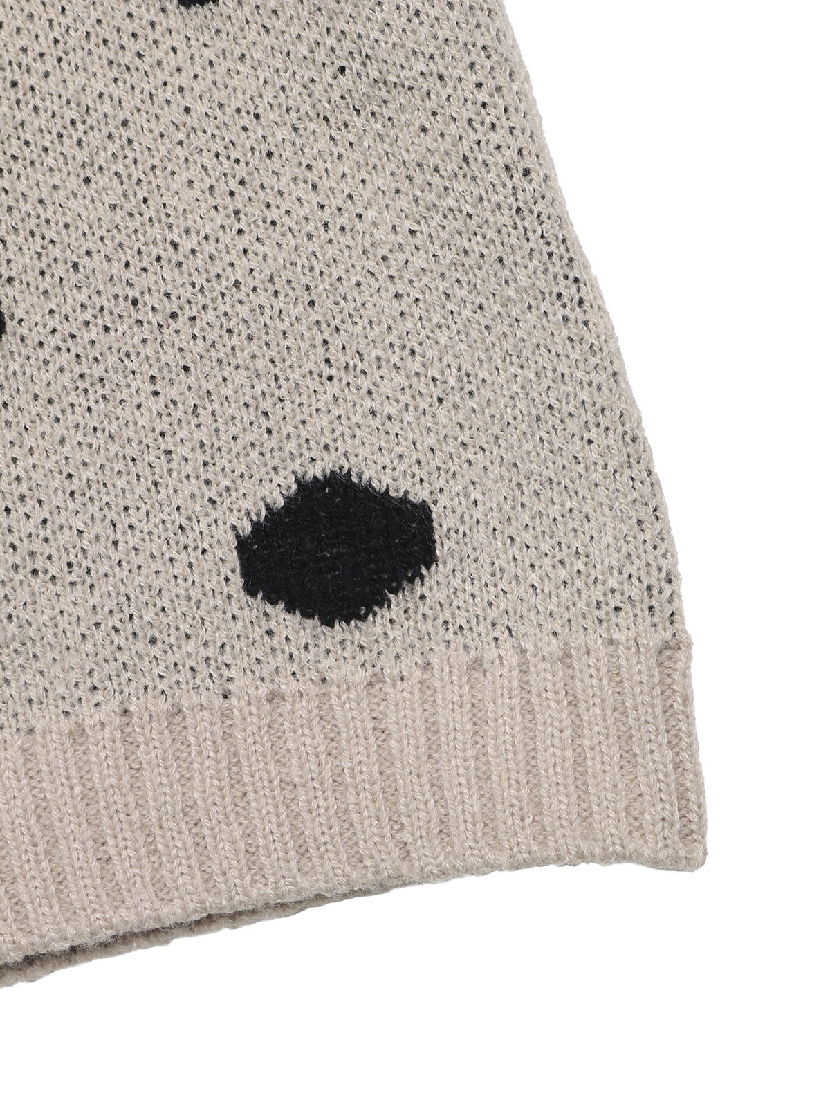 Close-up of a knit beanie in a light oatmeal beige color with black knit polka dots and a ribbed cuff, shown on a plain white background.