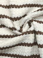 A close-up of a textured knit fabric with horizontal stripes in dark brown and off-white, styled with a central swirl.
