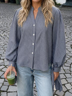 A woman wearing a navy and white gingham button-up shirt with voluminous sleeves, paired with light-wash blue jeans, standing outdoors on a cobblestone street and holding an iced green drink.