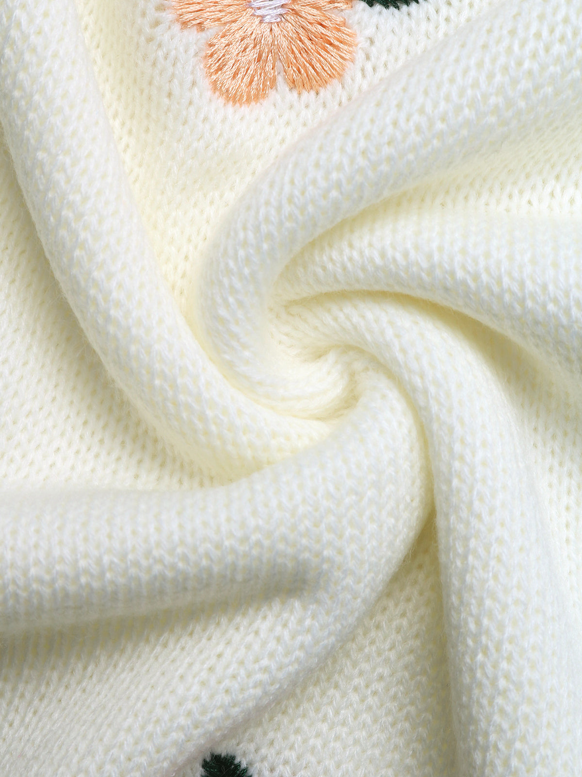 Close-up of a cream-colored knit fabric with a textured swirled drape and a peach embroidered flower detail.