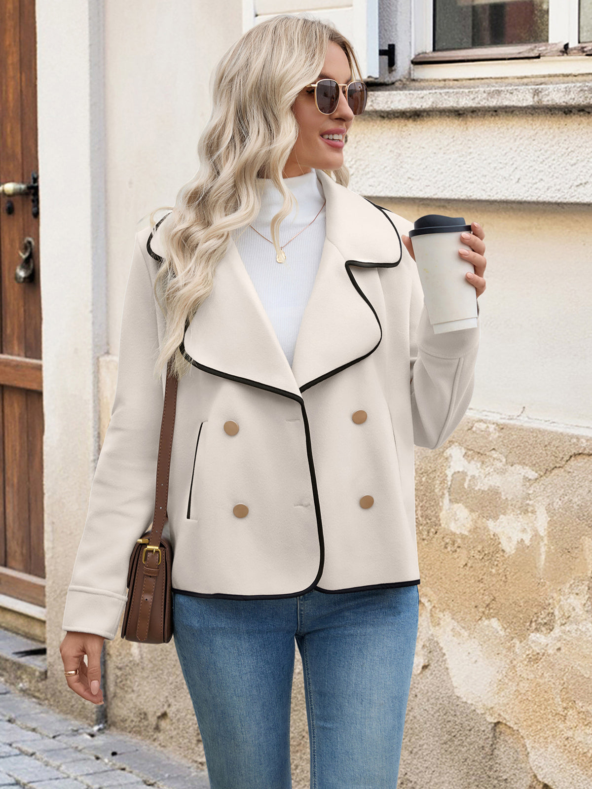 Woman in a beige jacket holding a coffee cup against a building background