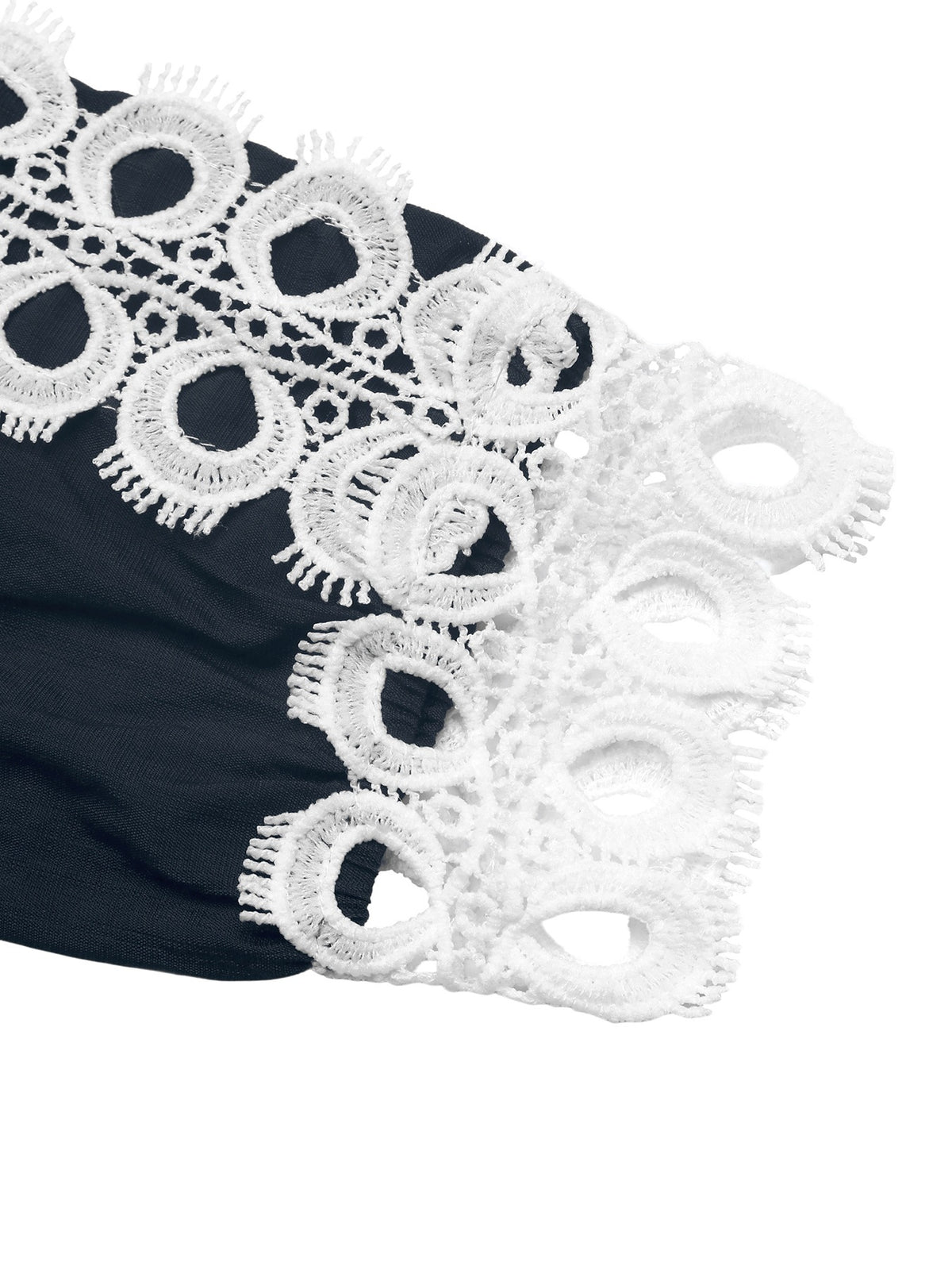 A close-up of a black garment featuring a wide white eyelet lace trim with circular cutout patterns and fringed edges, shown against a plain white background.