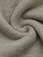 A close-up of a soft, knitted fabric in a light oatmeal beige color, arranged in a gentle spiral drape to show texture and flexibility.
