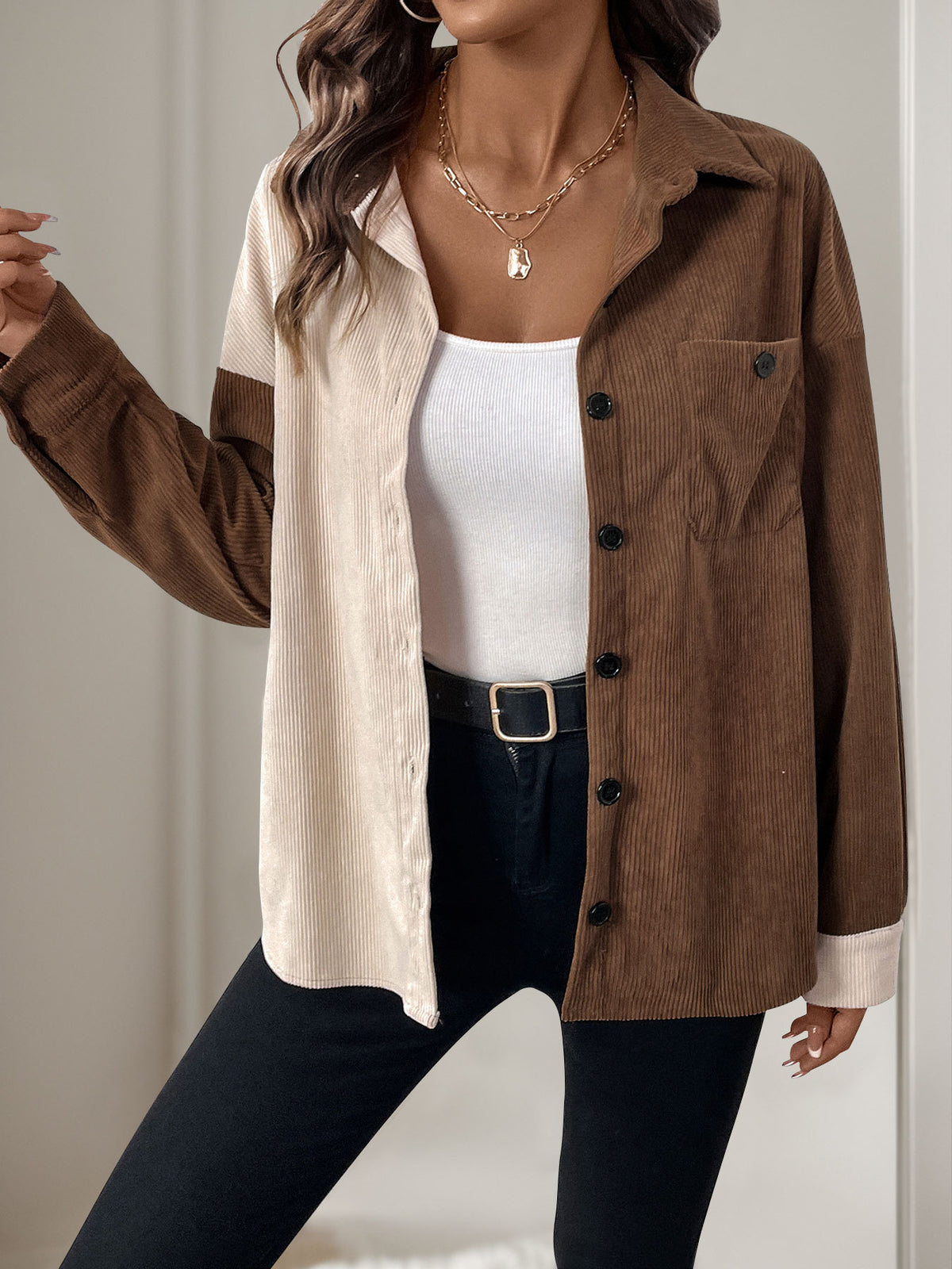 Woman wearing a brown and beige jacket over a white top and black pants.