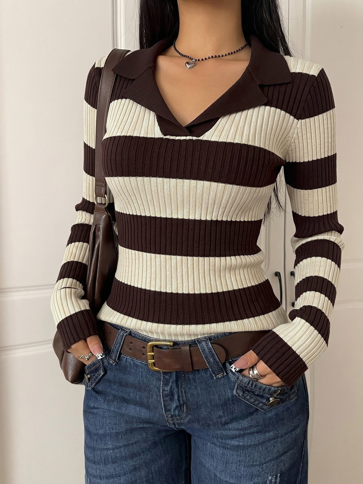 A woman wearing a brown and cream striped ribbed knit polo sweater, paired with blue jeans and a brown shoulder bag.