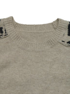 Close-up of a knit sweater showing the ribbed crew neck and shoulder details in a light taupe-beige color with black accents.