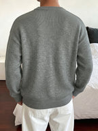 A person viewed from behind wearing a heather gray ribbed knit sweater and white pants in an indoor room setting.