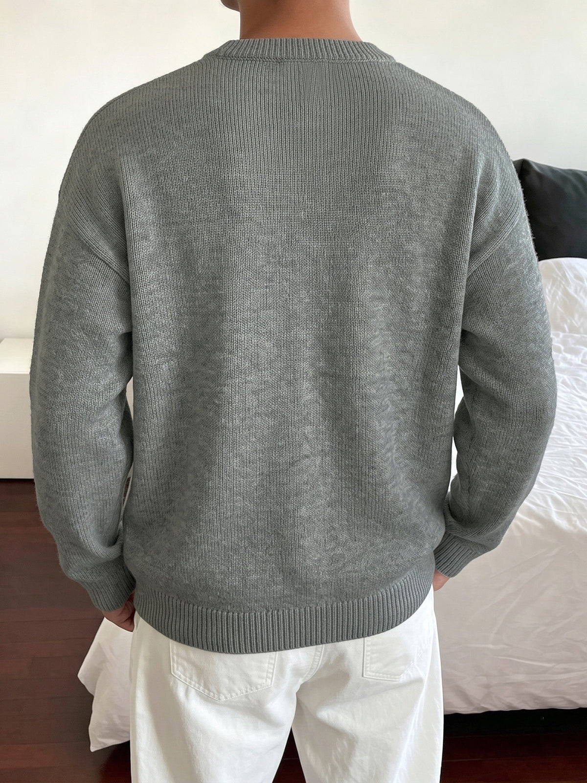 A person viewed from behind wearing a heather gray ribbed knit sweater and white pants in an indoor room setting.