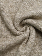 A close-up of a soft, knitted fabric in a warm light beige or oatmeal color, arranged in a spiral drape to show texture and flexibility.
