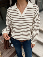 A woman wearing a cream and brown horizontally striped knit polo sweater, paired with blue jeans and holding a brown handbag.