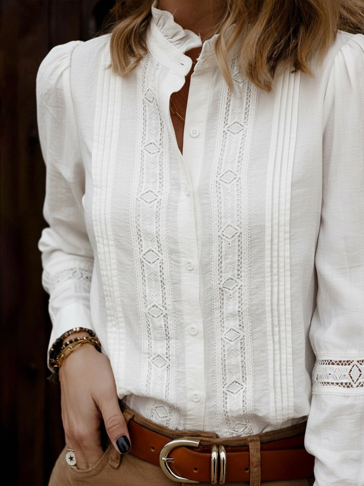 Close-up of a person wearing a white embroidered blouse with a brown belt.