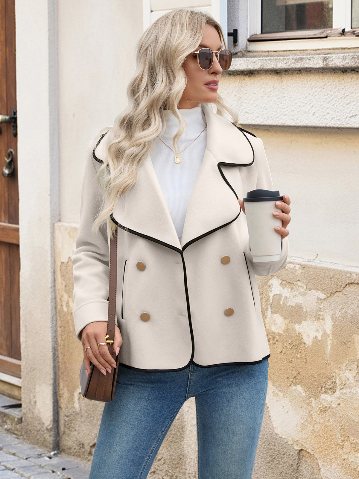 Woman in a beige jacket holding a coffee cup on a street.