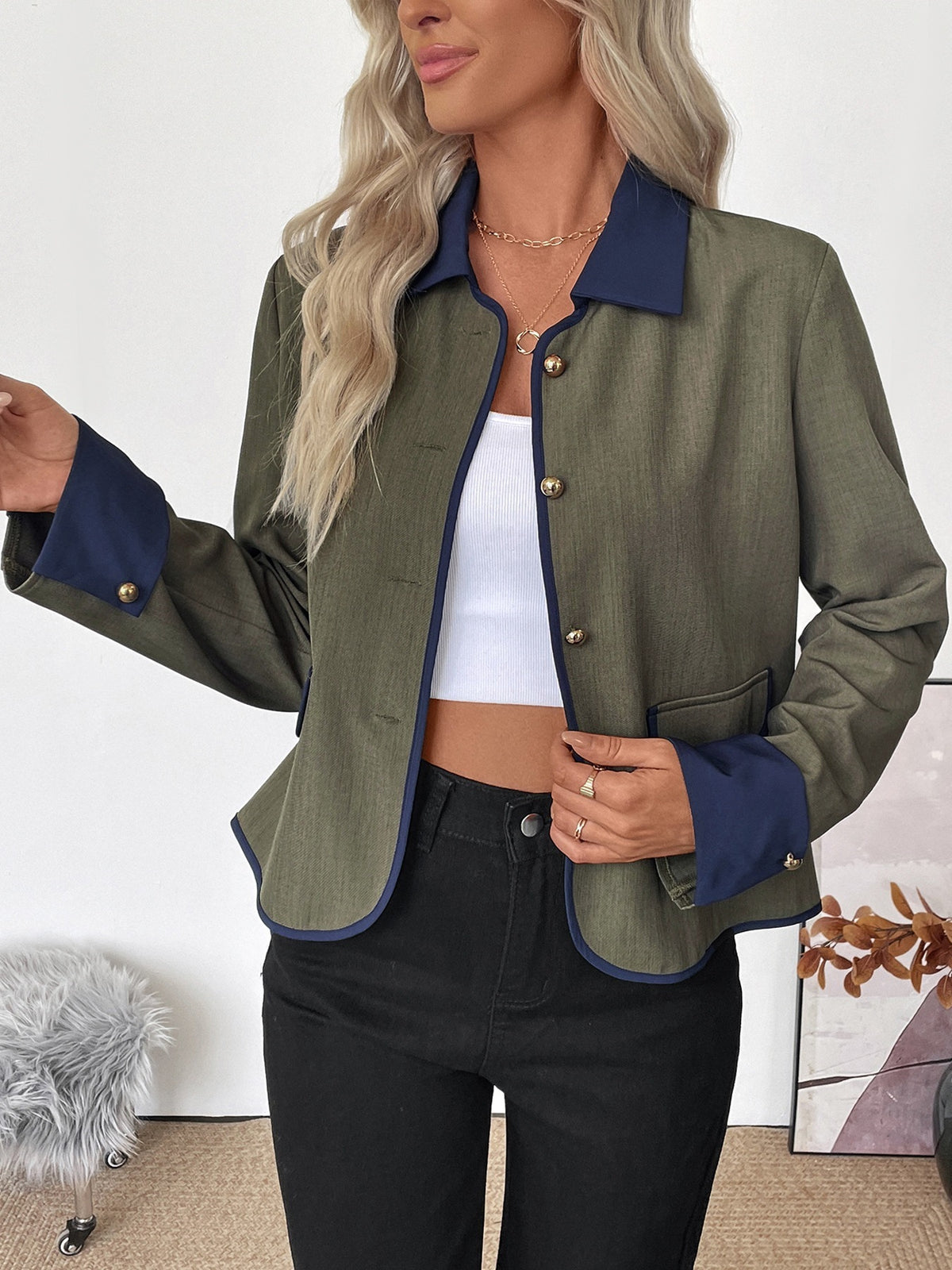 Woman wearing a green jacket with blue trim and black pants indoors.