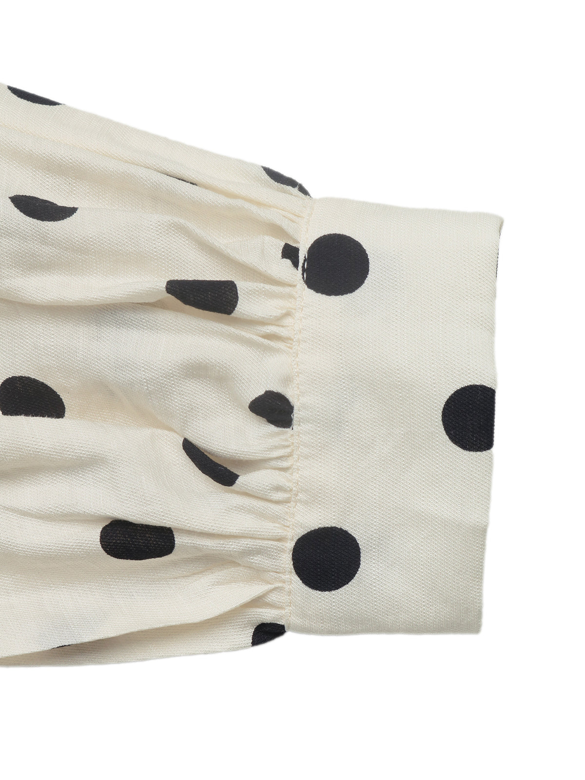 Close-up of a cream-colored fabric garment with black polka dots and a gathered cuff, shown against a plain white background.
