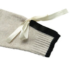 A close-up of a cream-colored knit sleeve with a black ribbed cuff and a cream satin ribbon tied in a bow, set against a plain white background.